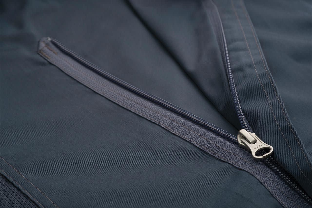 A close-up of a dark navy chef jacket featuring a zippered pocket detail. The fabric appears smooth and durable.