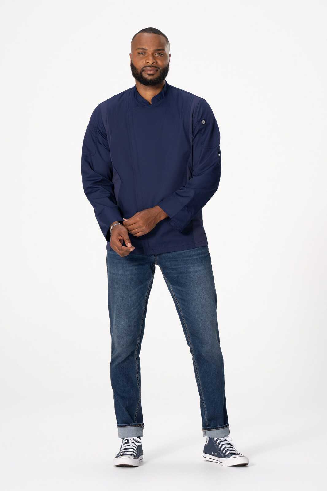 A navy blue men's chef jacket worn by a model, paired with blue jeans and casual shoes. Features branding.