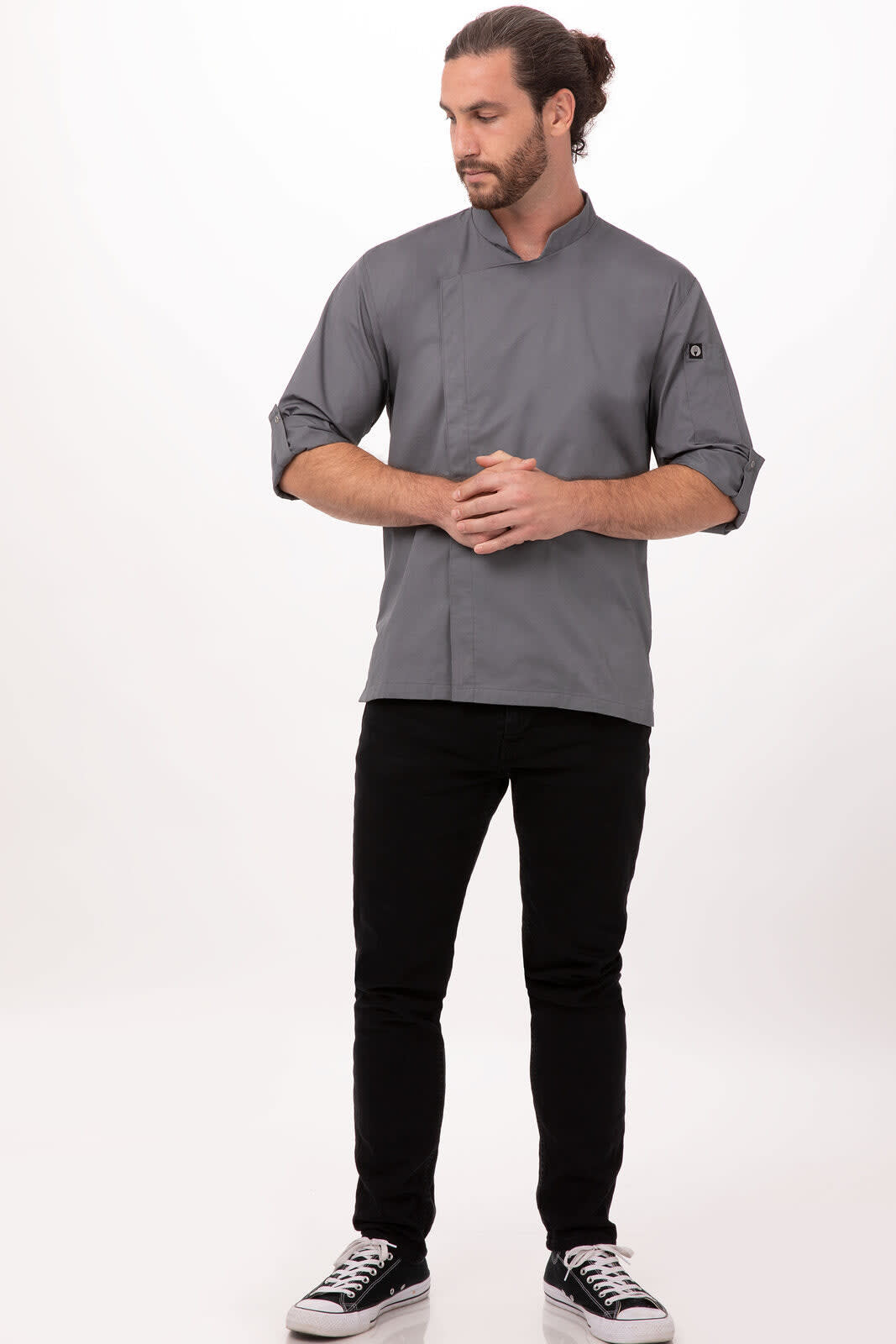 A grey chef jacket worn by a man, paired with black pants and sneakers, featuring a logo on the sleeve.