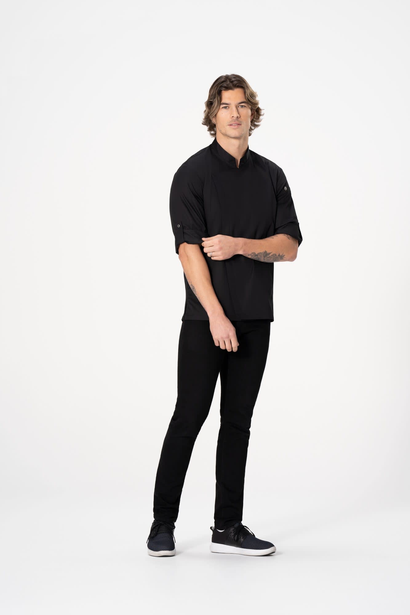 A model wearing a black chef jacket paired with black pants, standing against a white background.