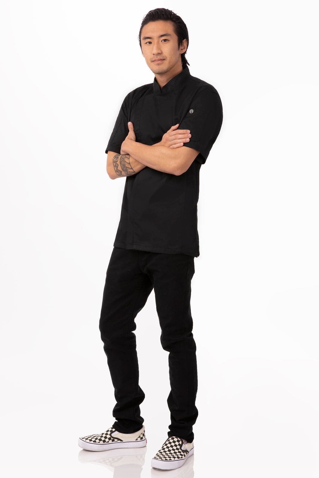 A black chef jacket worn by a model, paired with black jeans and checkered shoes, featuring a logo on the sleeve.