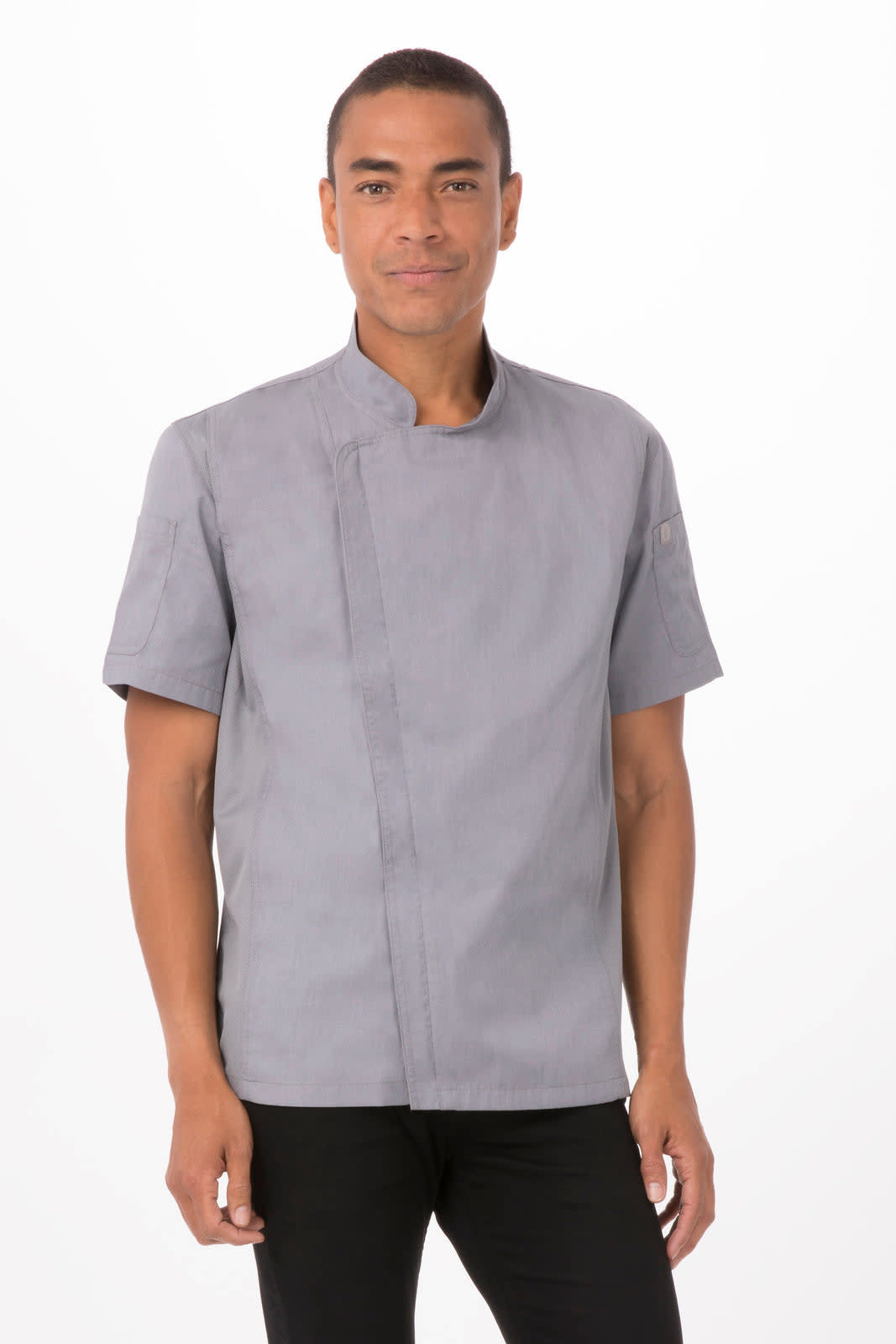 A man wears a short-sleeved, grey chef jacket with a logo on the sleeve, posing confidently.