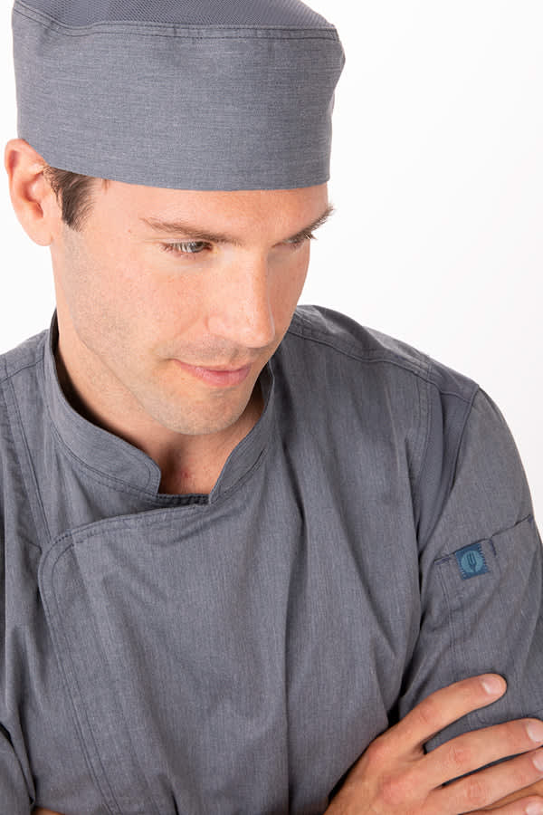 A grey chef jacket modelled by a man wearing a matching grey hat, featuring a logo on the sleeve.