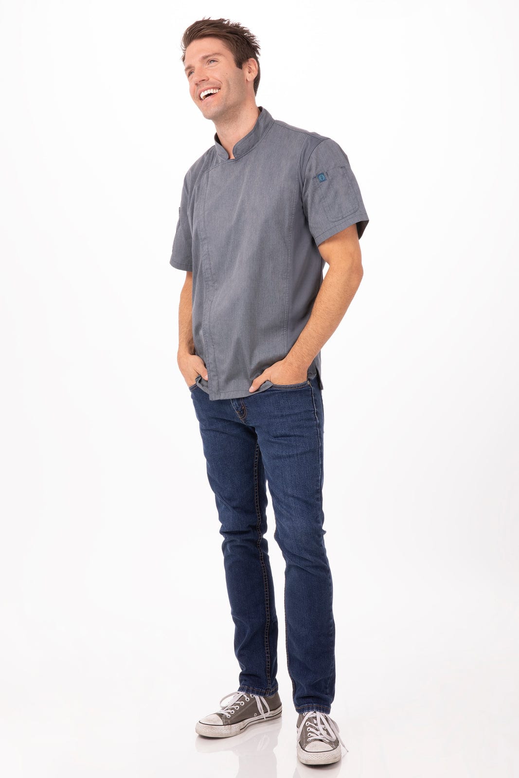 A man wearing a grey chef jacket with a logo, paired with blue jeans and casual shoes.