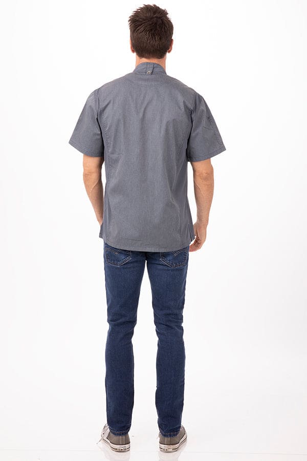 A grey men's chef jacket viewed from the back, paired with blue jeans and casual shoes. The jacket features a logo.