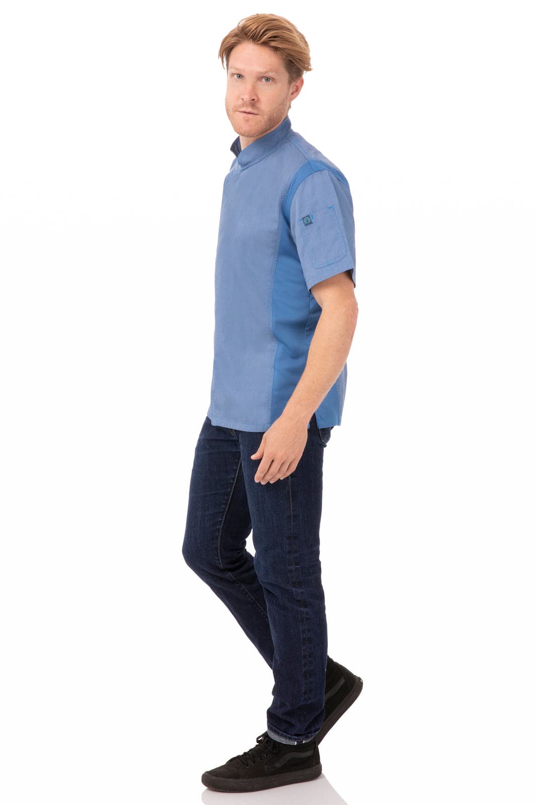 A man wearing a light blue chef jacket paired with dark jeans and black shoes, standing in a neutral pose.