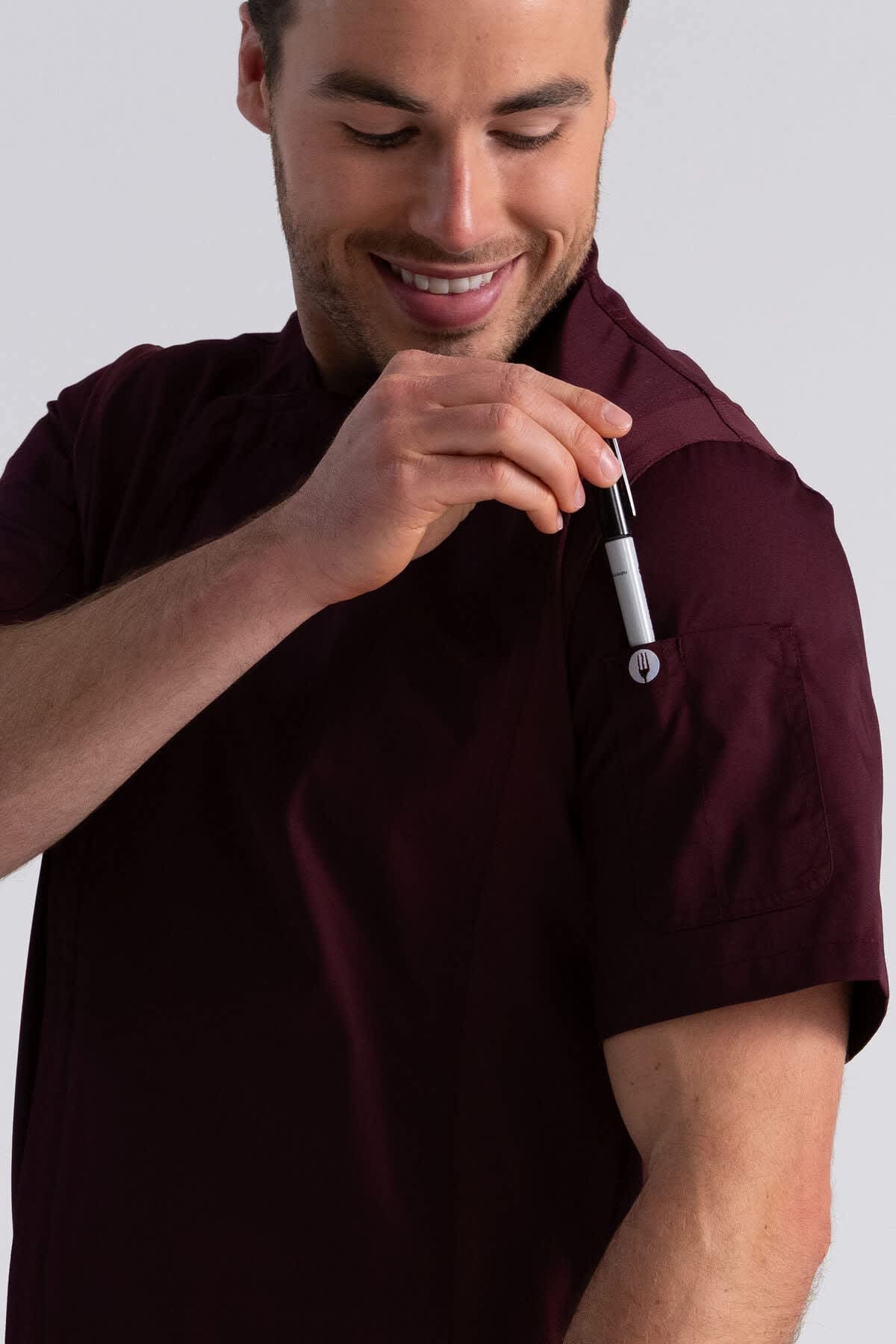 A burgundy chef jacket with short sleeves, featuring a pocket on the arm for holding a pen or utensil.
