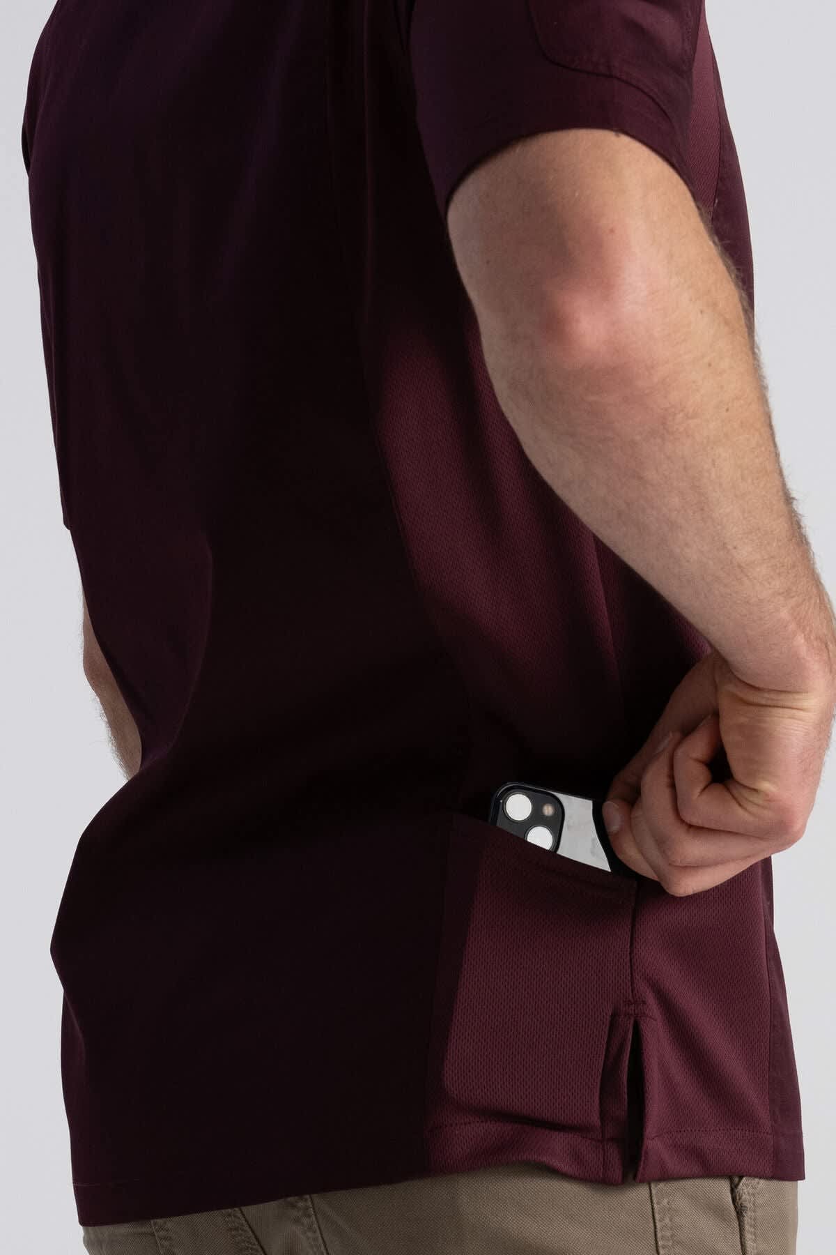 A maroon chef jacket with a pocket, styled on a model placing a phone inside. Features a logo on the jacket.