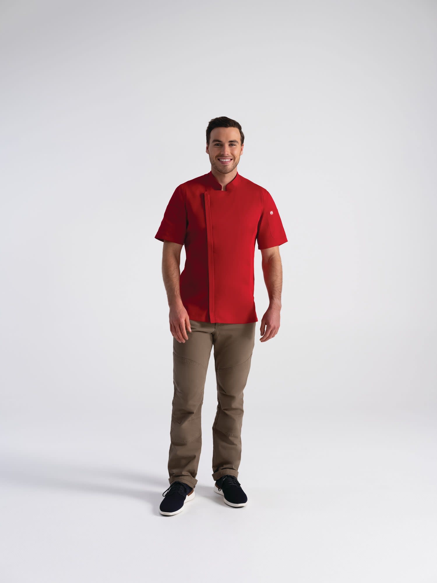 A man models a red chef jacket with short sleeves, paired with beige pants and black shoes. The jacket features a logo.