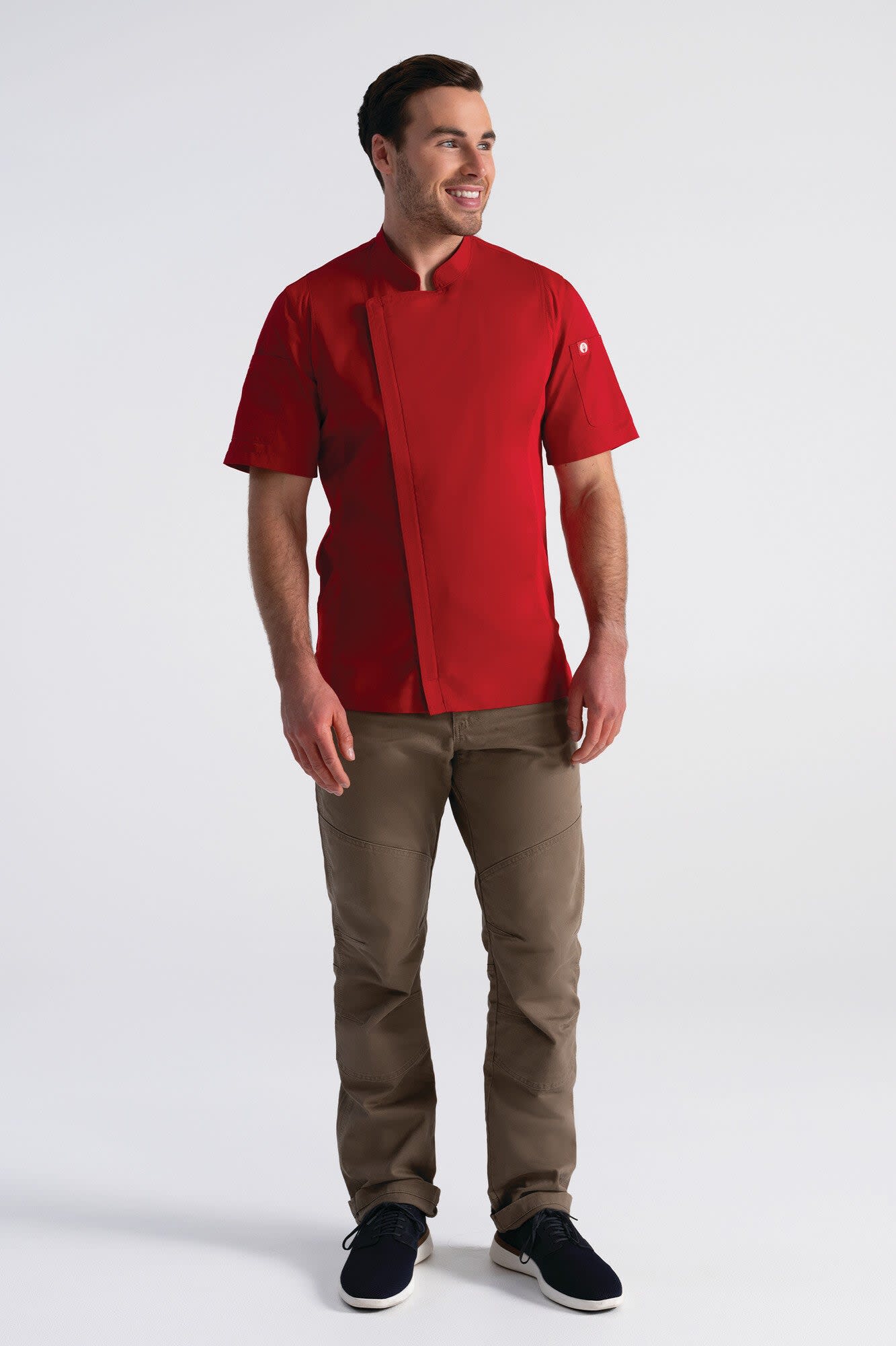 A man wearing a red chef jacket and brown pants, standing against a plain background. The jacket features a logo.