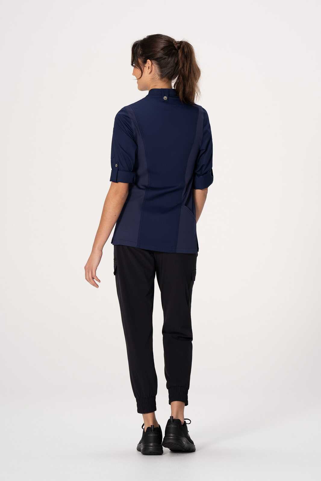 A women's chef jacket in navy with a logo, featuring a tailored fit and rolled sleeves, worn with black pants.