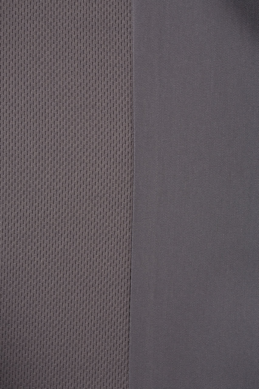 A grey chef jacket featuring both textured and smooth fabric panels, with a logo on one side.