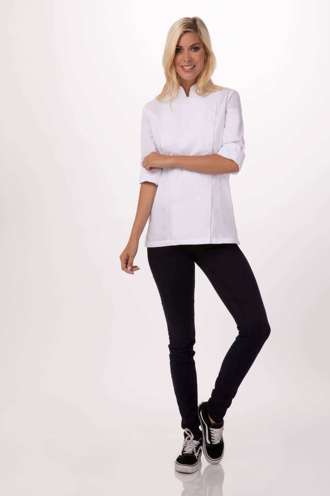A stylish white women's chef jacket with a modern design paired with black pants and sneakers, featuring a logo.