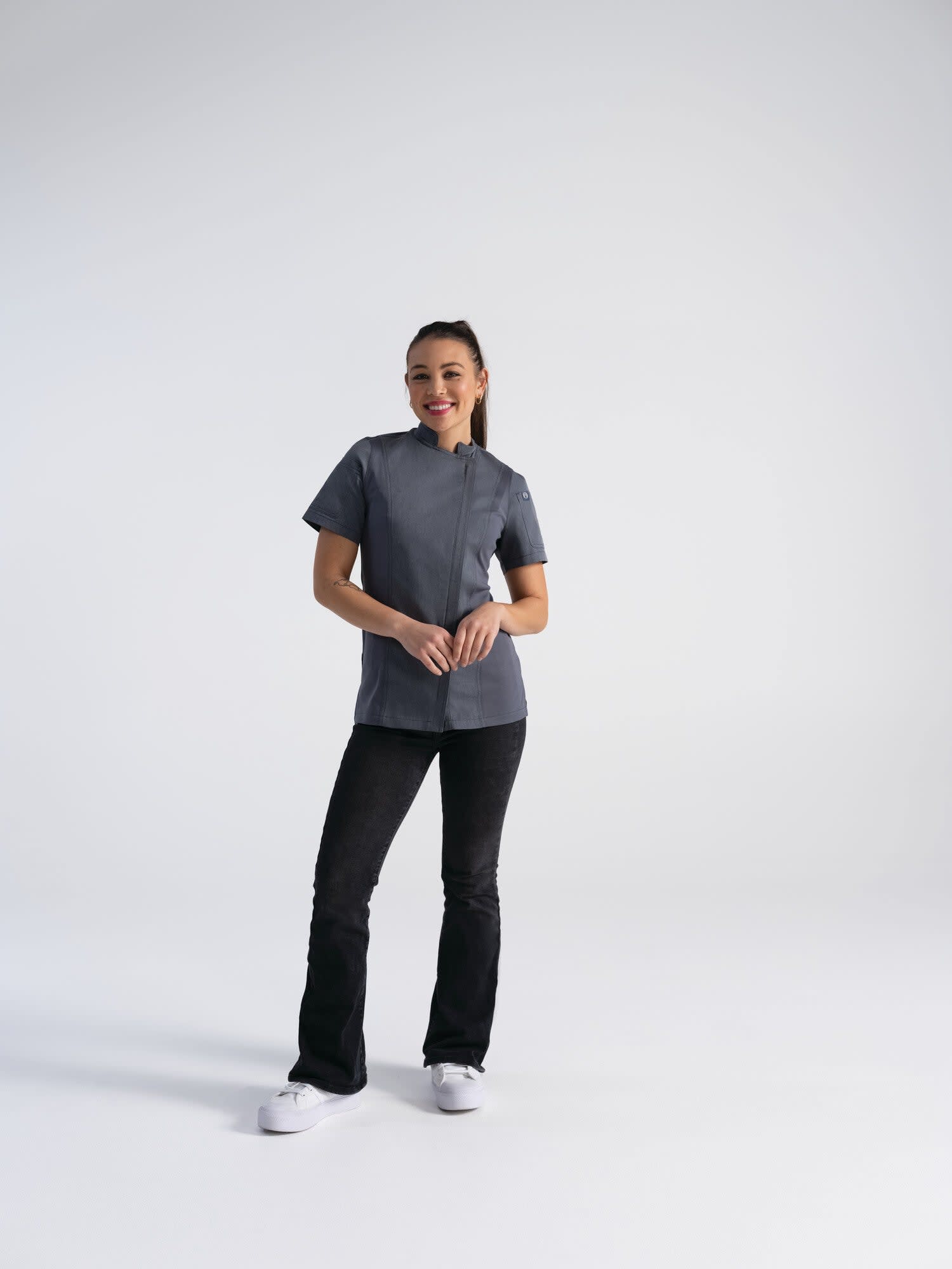 A chef jacket in grey, featuring short sleeves, worn by a woman paired with black pants and white shoes.