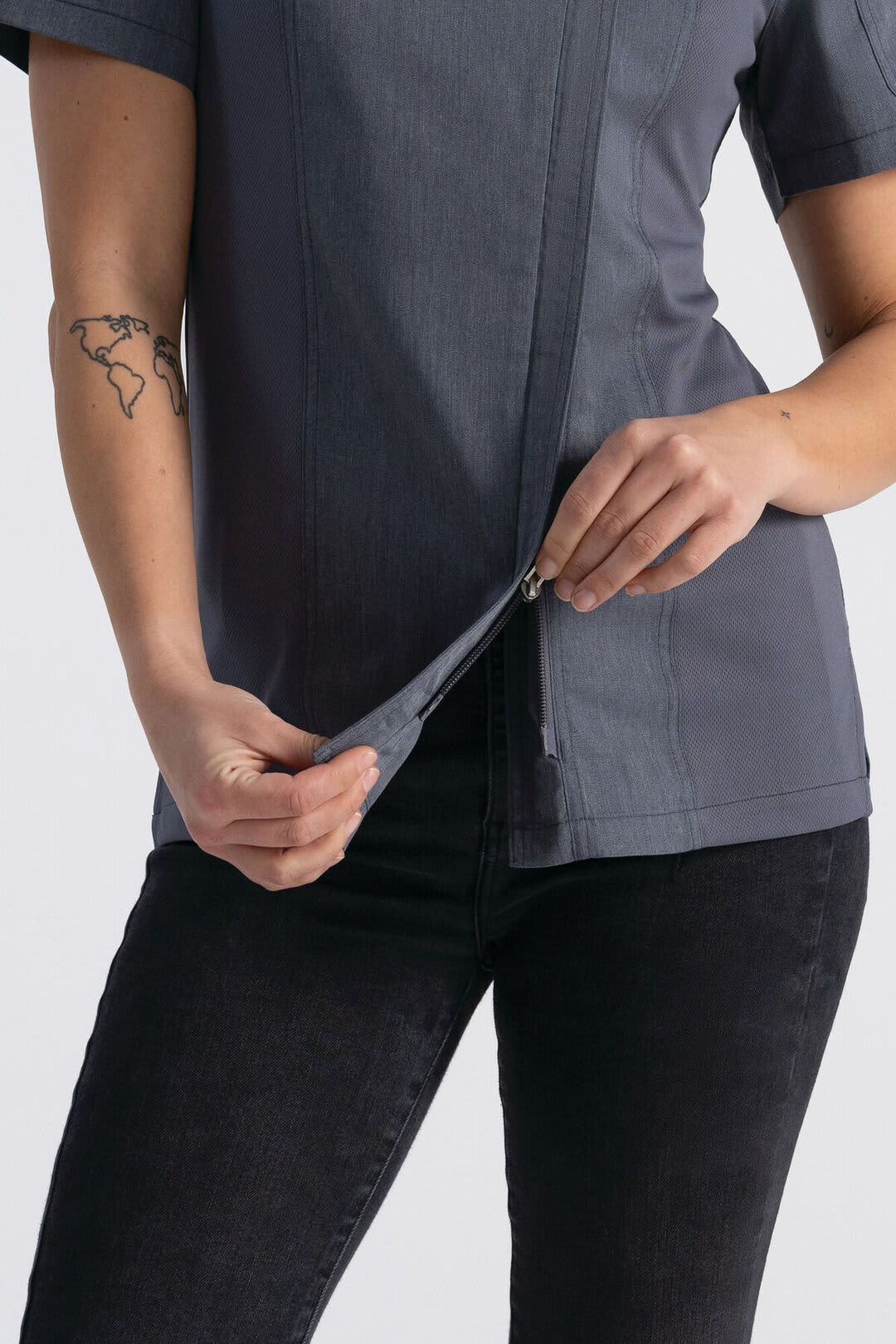 A women's chef jacket in grey, featuring a zip closure and short sleeves, showcased by a model holding the hem.