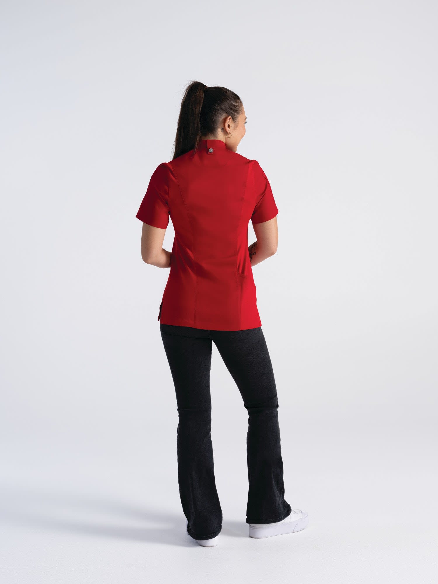 A woman wearing a red chef jacket, standing with her back to the camera, paired with black pants.