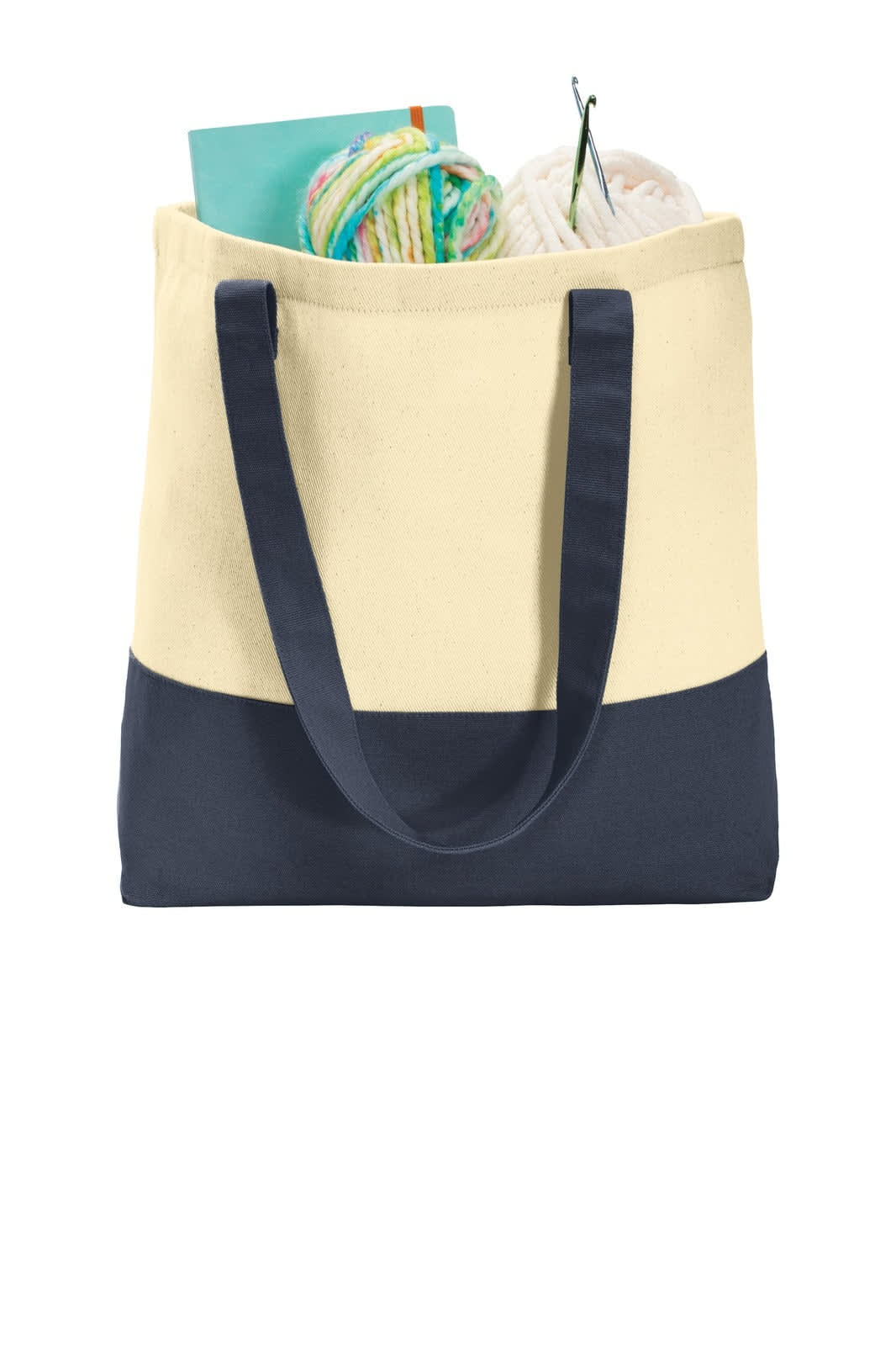 A cream and navy tote bag filled with yarn, knitting tools, and a notebook. Features a logo on the front.