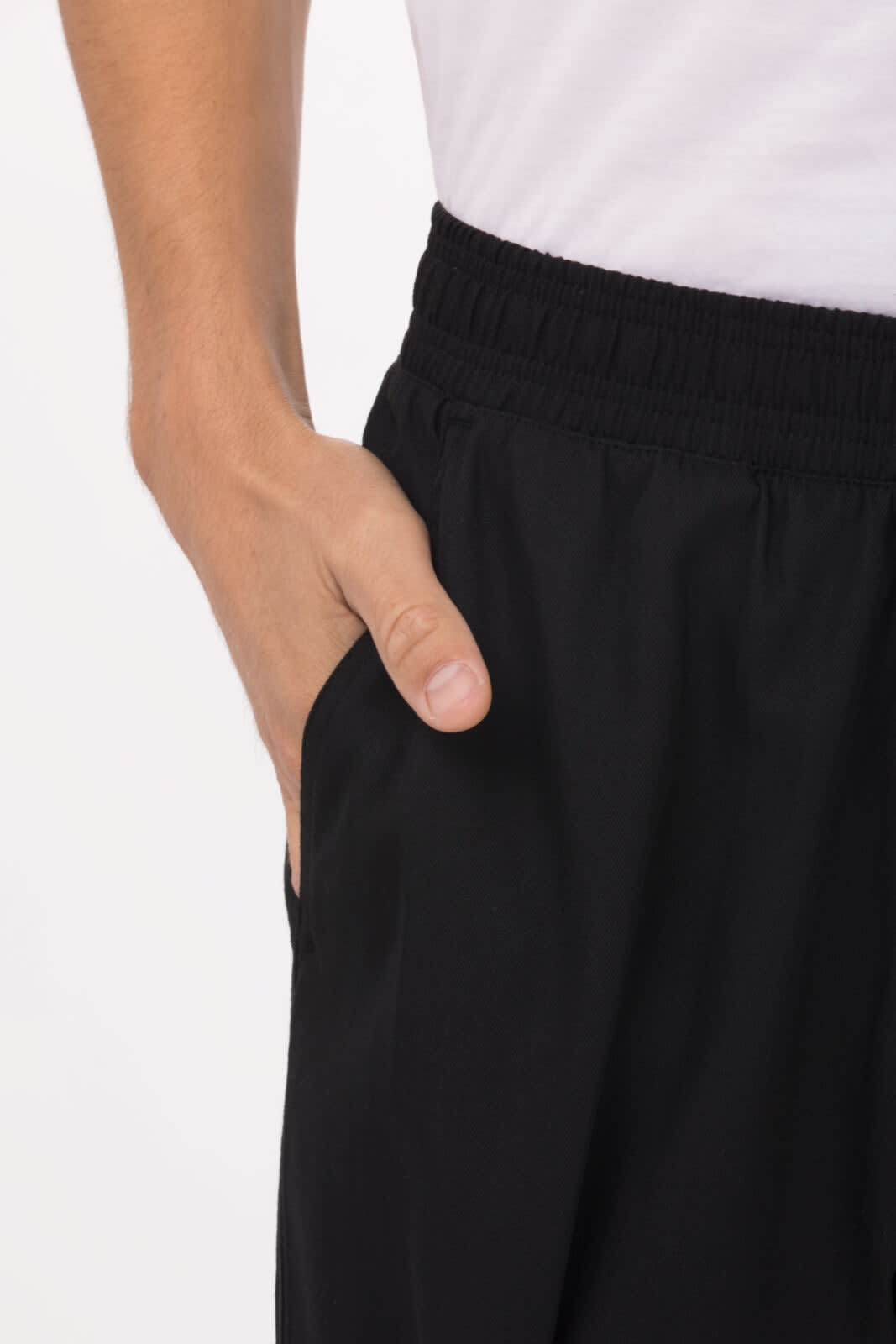 Close-up of black baggy chef pants with an elastic waistband and hand in pocket. Features a logo on the waistband.