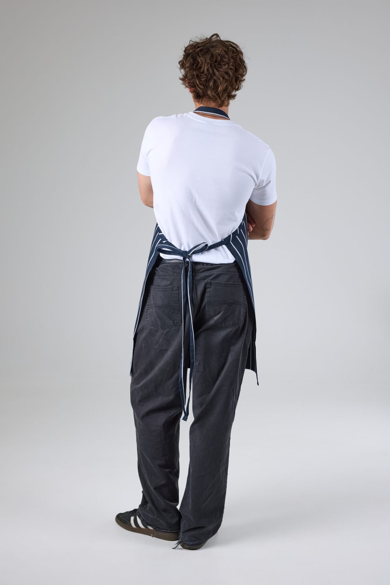 A blue and white striped bib apron worn by a person facing away, paired with grey pants and black shoes.