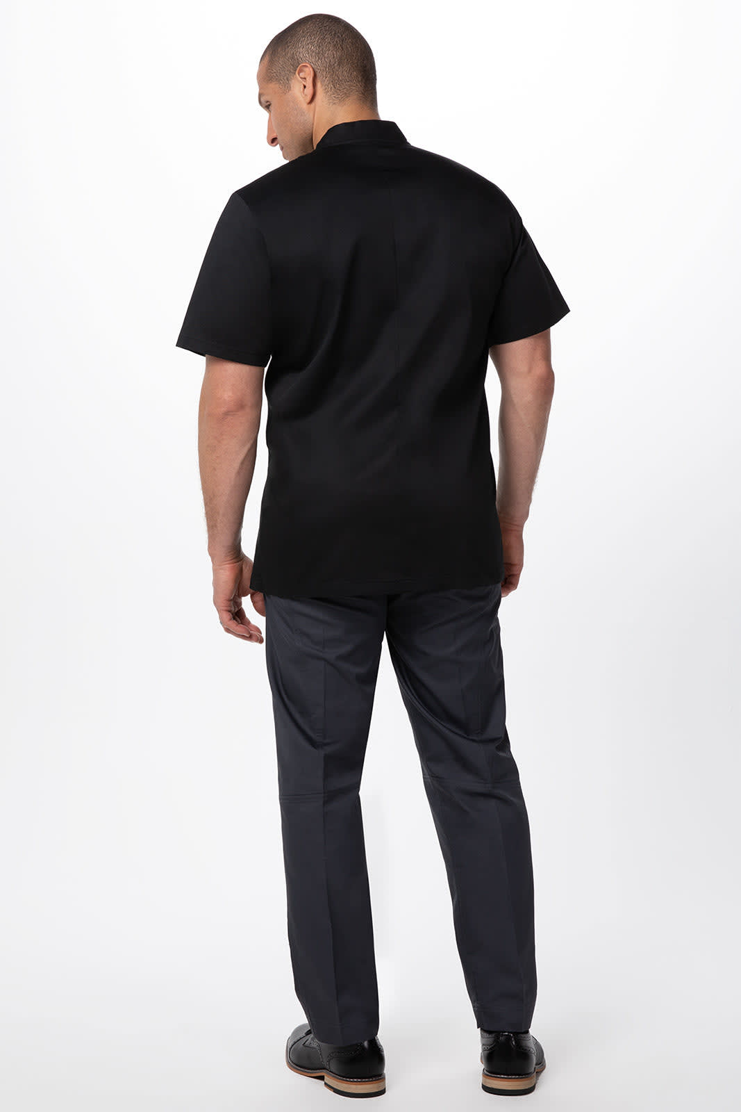 A men's black chef jacket with short sleeves, shown from the back, paired with dark trousers. Features a logo.