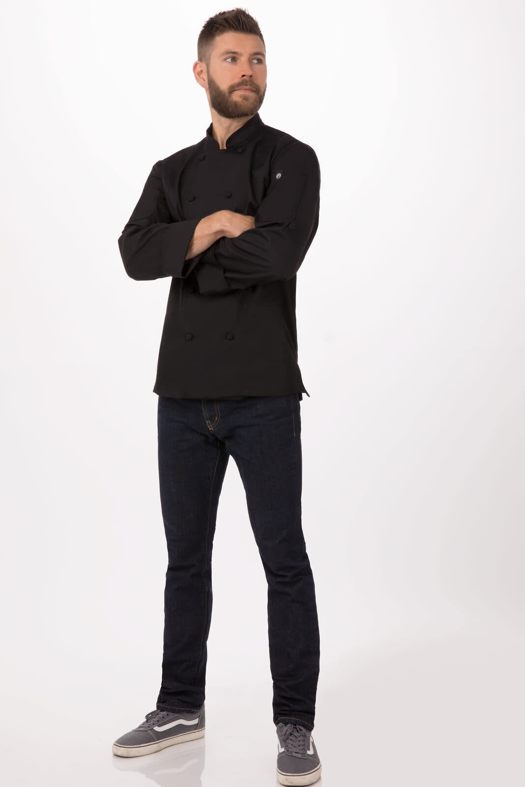 A men's chef jacket in black worn by a model, paired with dark jeans and grey shoes. The jacket features a logo.