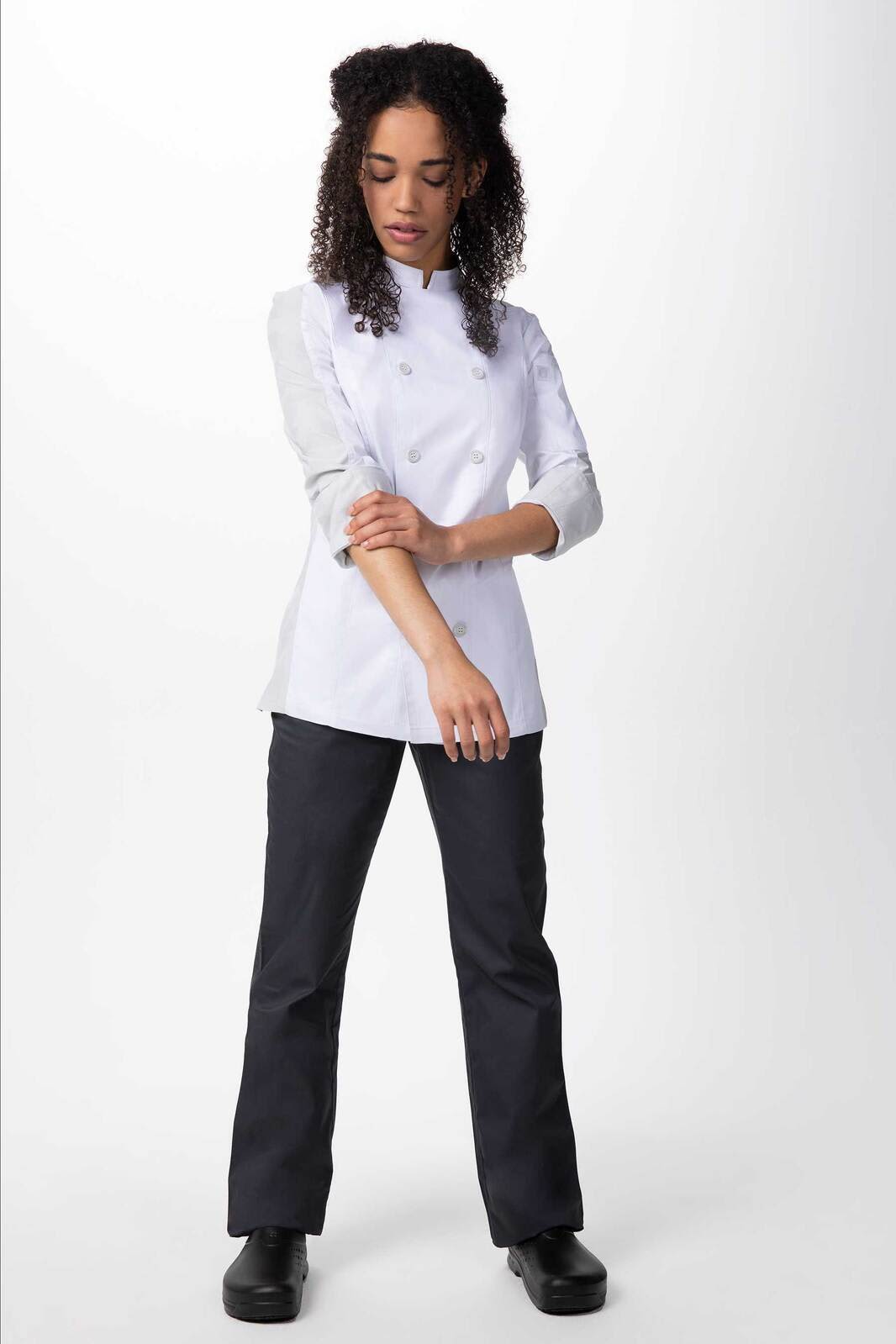 A white women's chef jacket paired with black pants, featuring long sleeves and a tailored fit. It has a logo on the jacket.