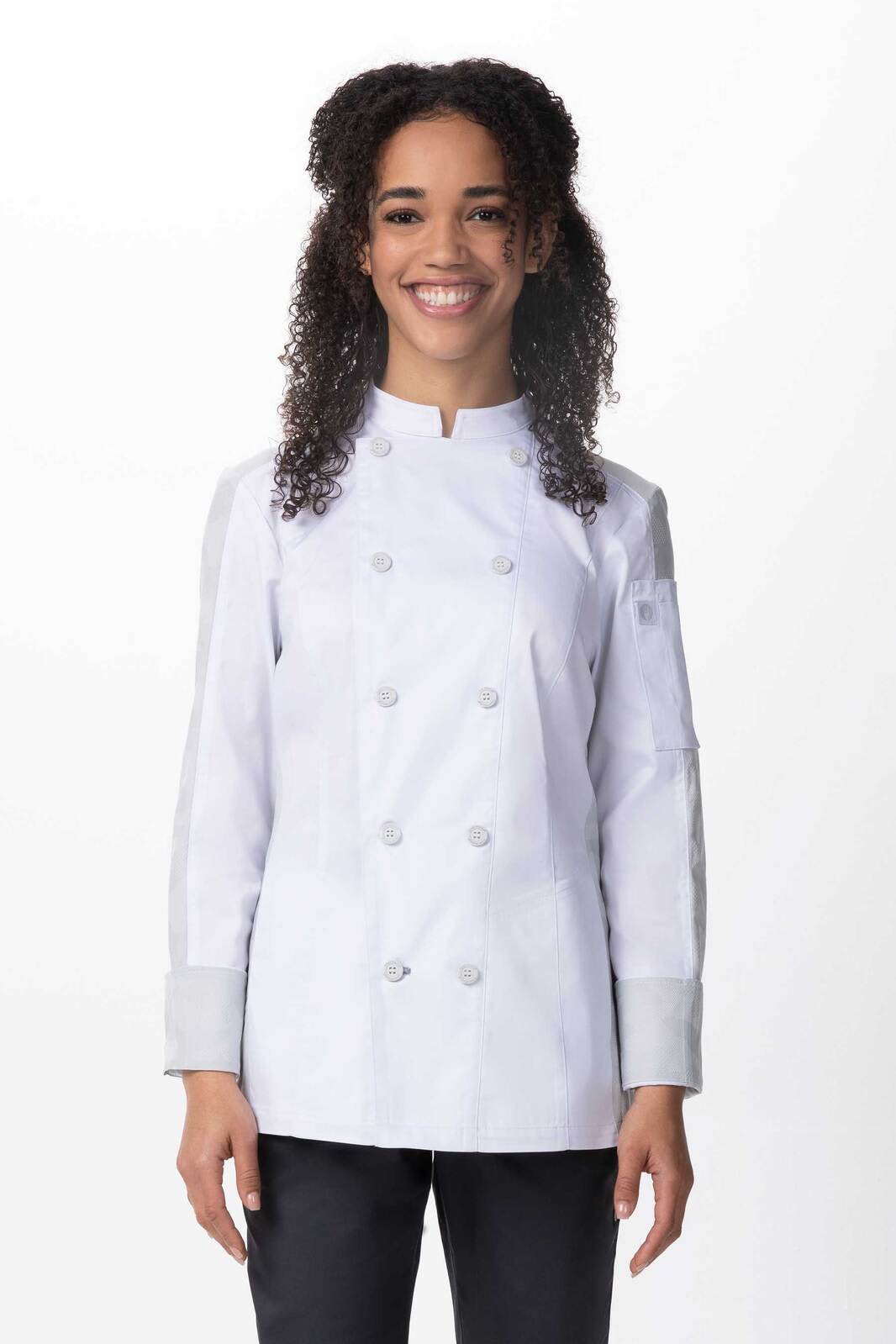 A woman smiling in a white chef jacket with grey accents, featuring a branded logo on the sleeve.