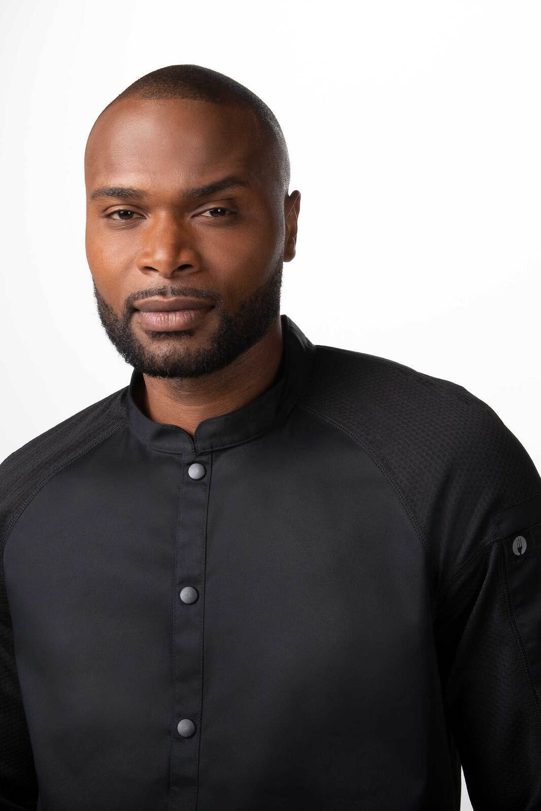 A men's chef jacket in black with a button-up front and textured sleeves, featuring a logo on the sleeve.