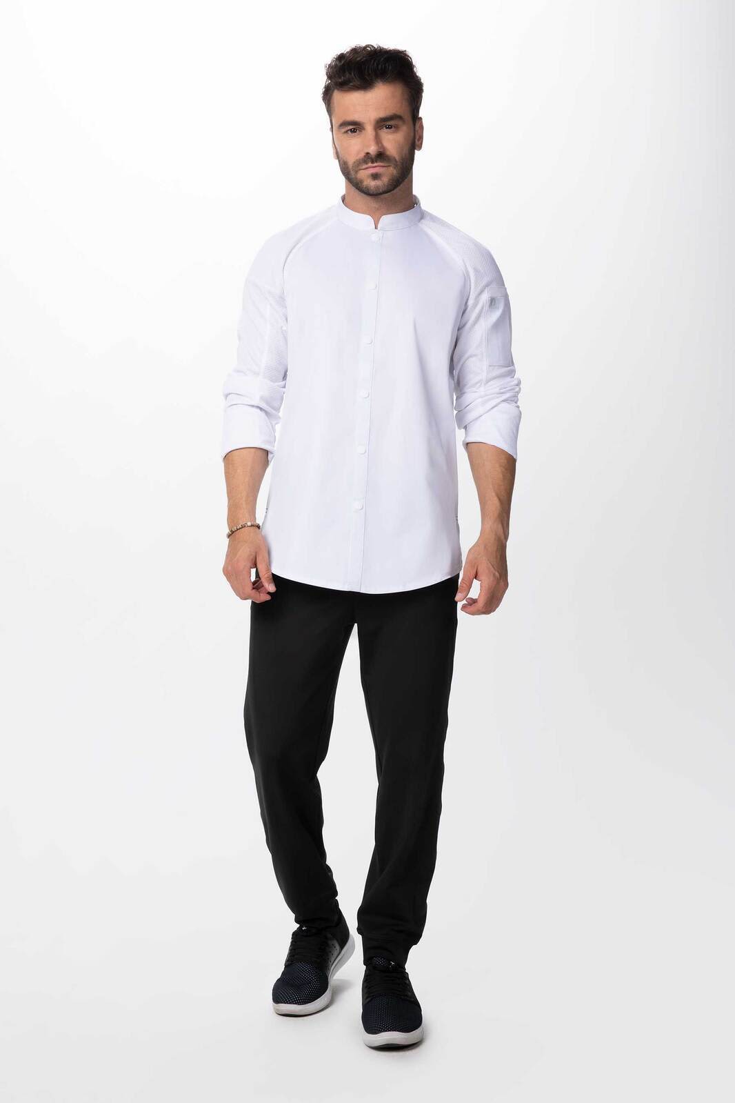 A man wearing a white chef jacket with a mandarin collar, paired with black trousers and shoes. The jacket has a logo.