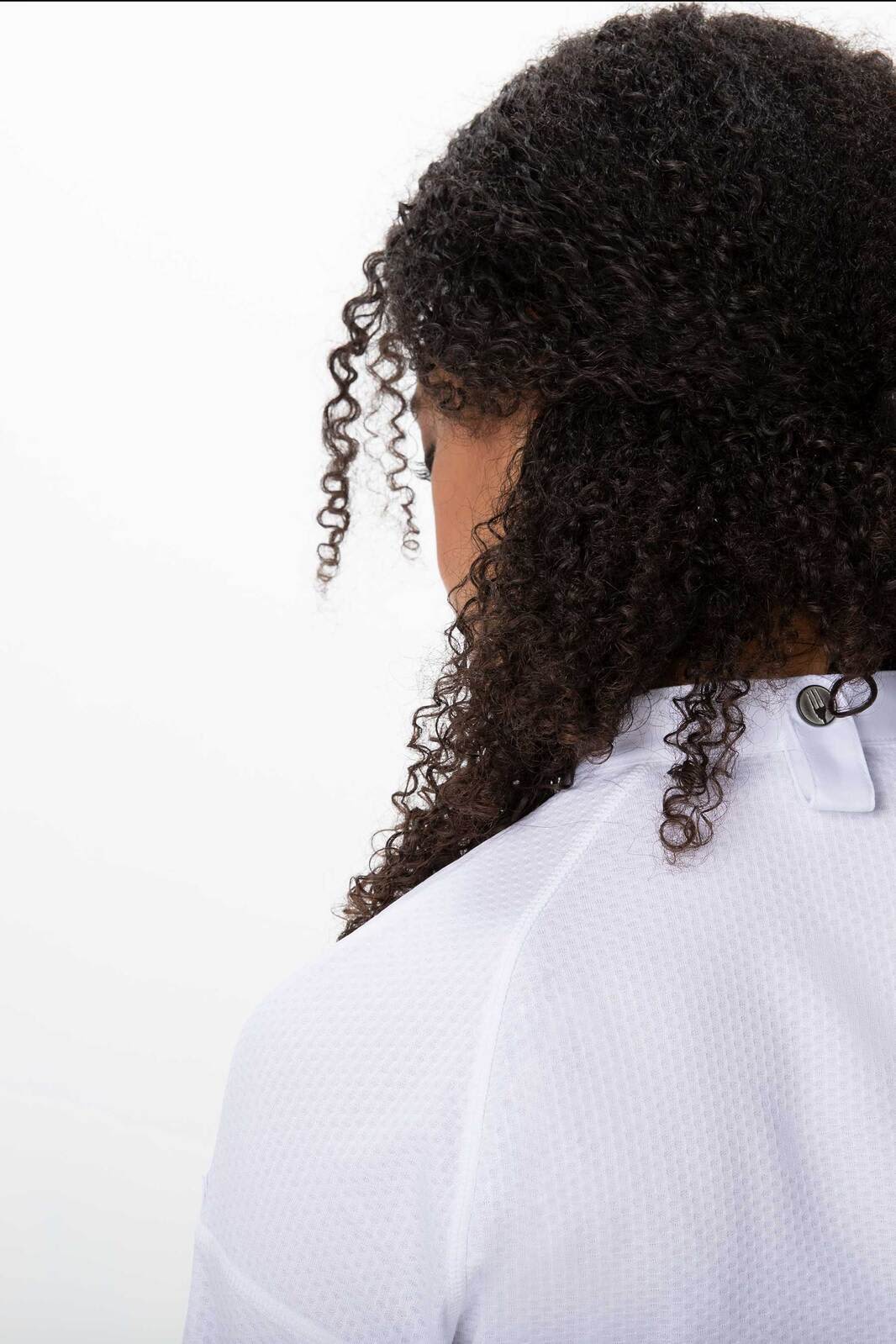 A white women's chef jacket featuring a back detail and a logo, shown from the back with curly hair visible.