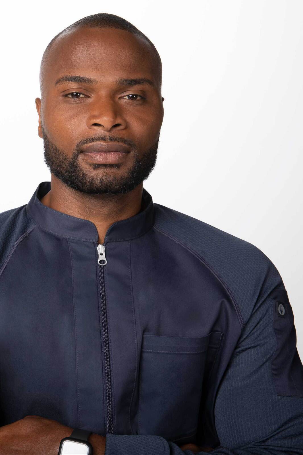 A dark navy chef jacket on a model, featuring a zip front and a chest pocket. It has a logo on the sleeve.