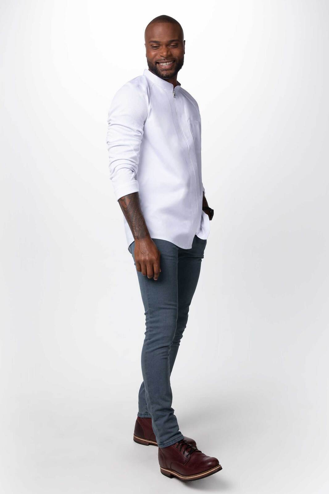 A men's chef jacket in white with a stand-up collar, paired with slim-fit grey trousers and brown shoes.