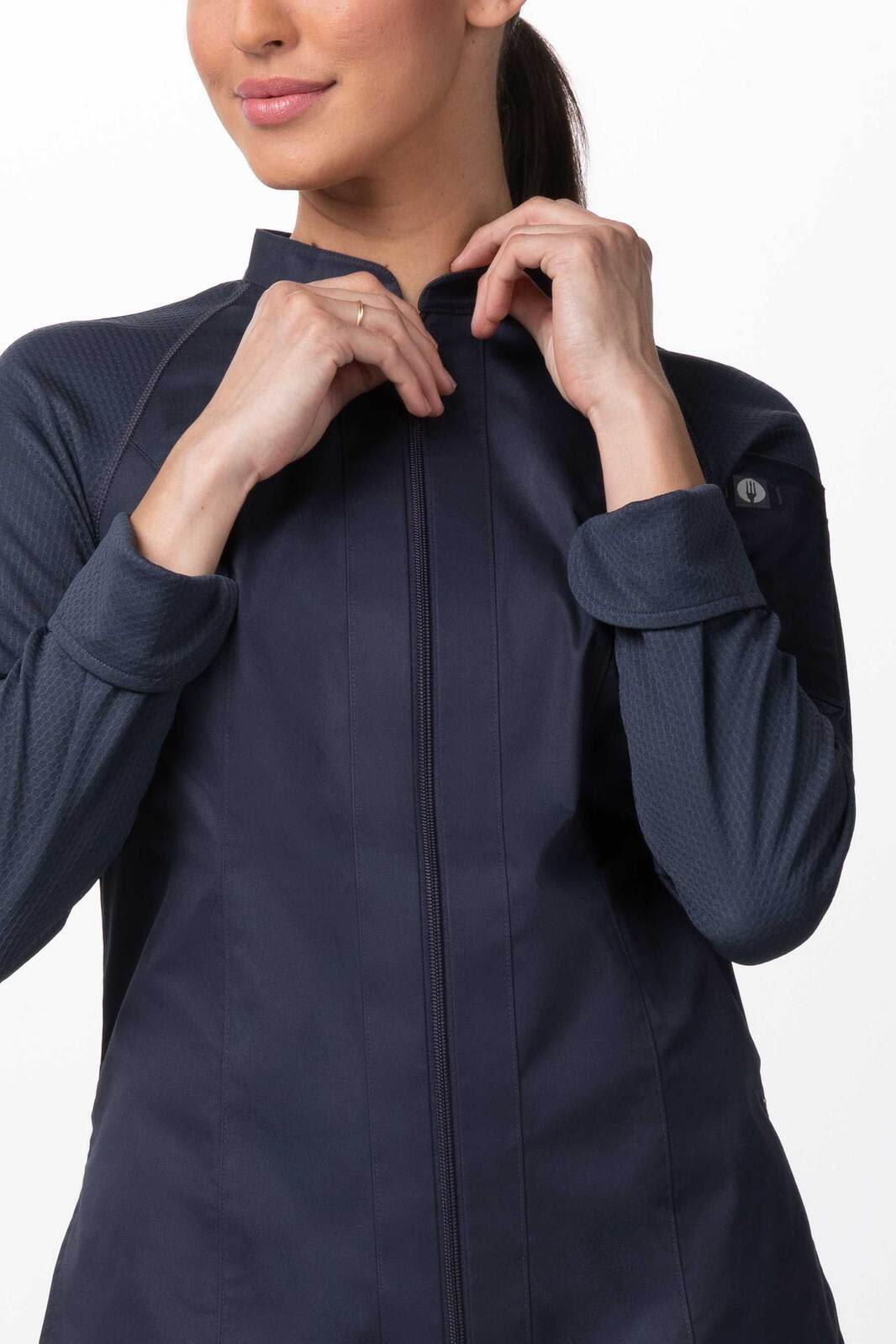 A navy women's chef jacket featuring a high collar and a logo on the sleeve. The model adjusts the jacket.