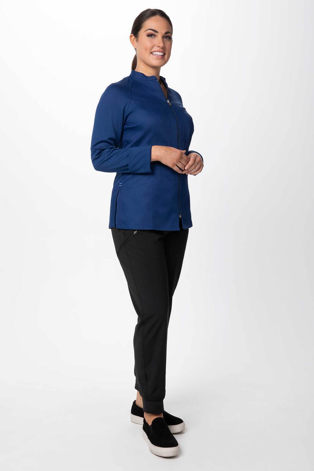 A women's chef jacket in navy, paired with black pants, worn by a model standing confidently. The jacket features a logo.