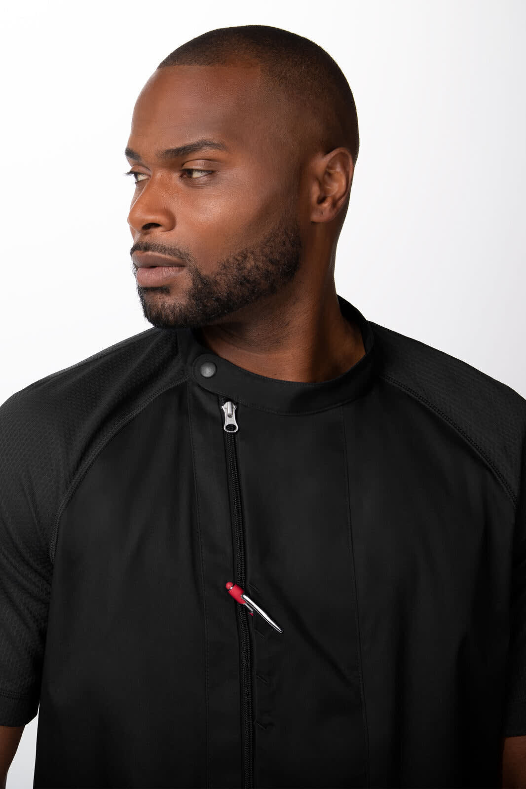 A black men's chef jacket featuring a zip and a pocket with a pen. The model poses with a serious expression.