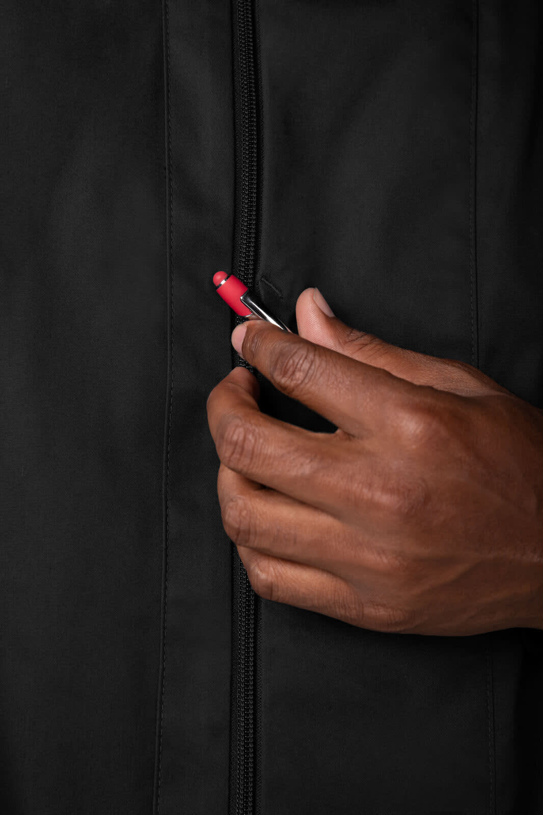 A black chef jacket with a close-up of a hand gripping the zipper, showcasing a red zip pull.