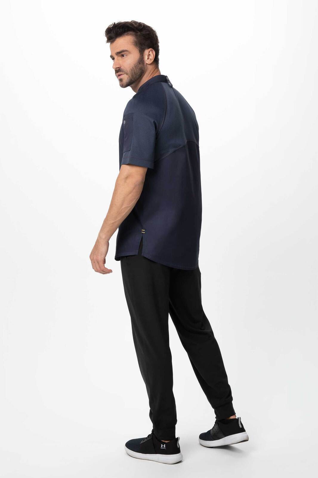 A men's chef jacket in navy blue, featuring a logo, worn with black pants and sporty shoes.