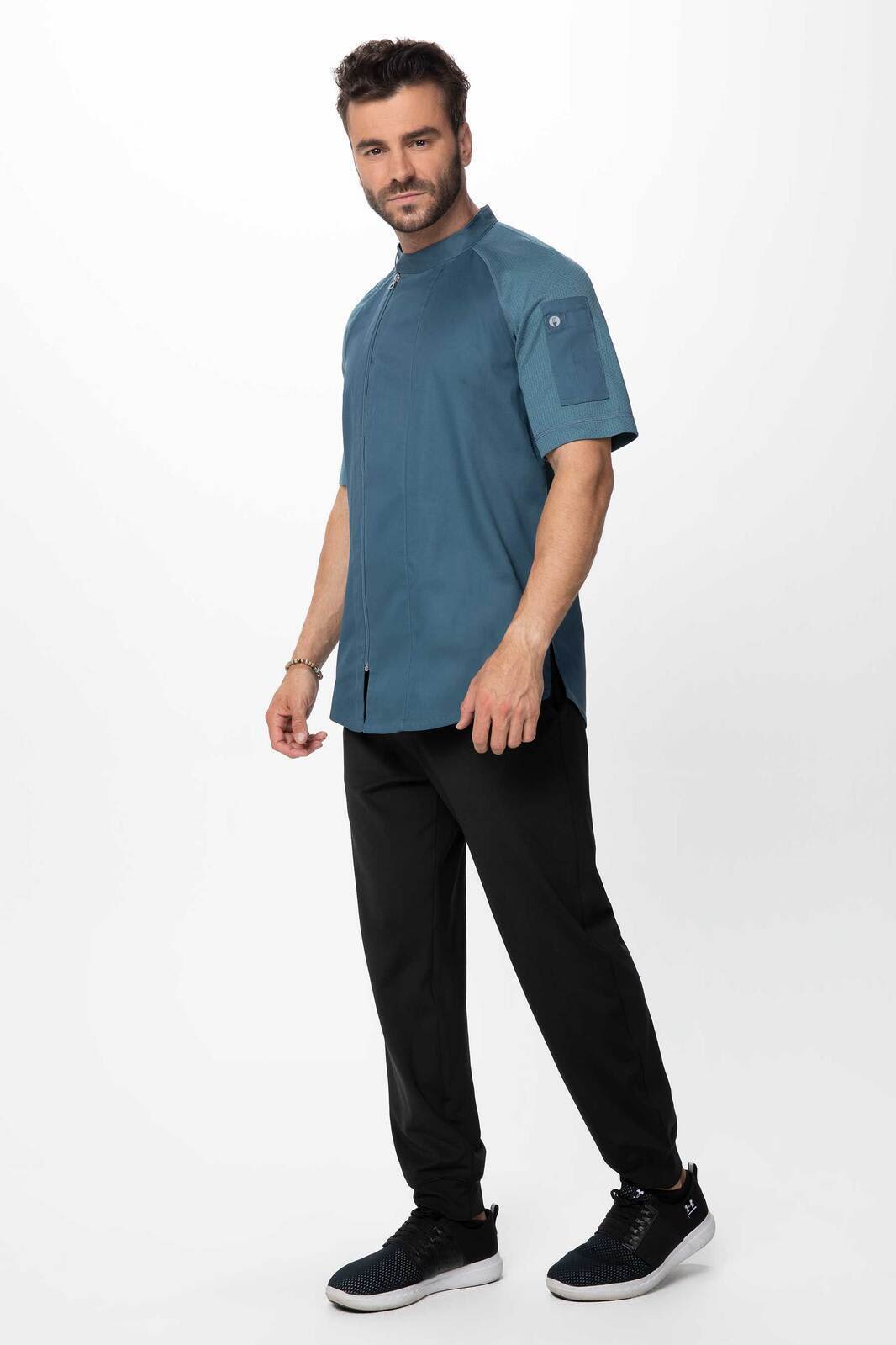 A men's chef jacket in teal, paired with black pants, featuring a logo on the sleeve.