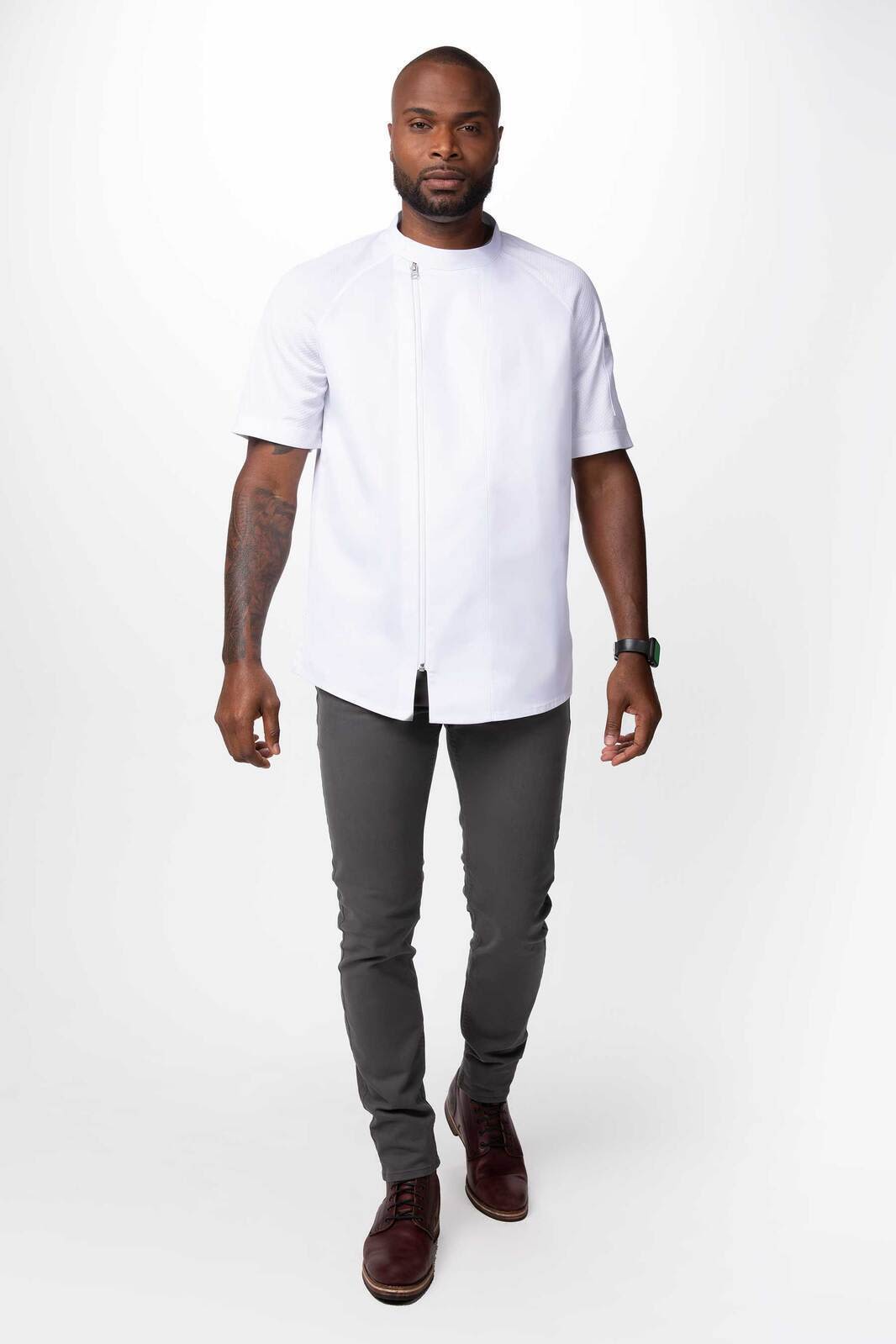 A man wearing a white chef jacket with short sleeves, paired with dark grey pants and dress shoes.