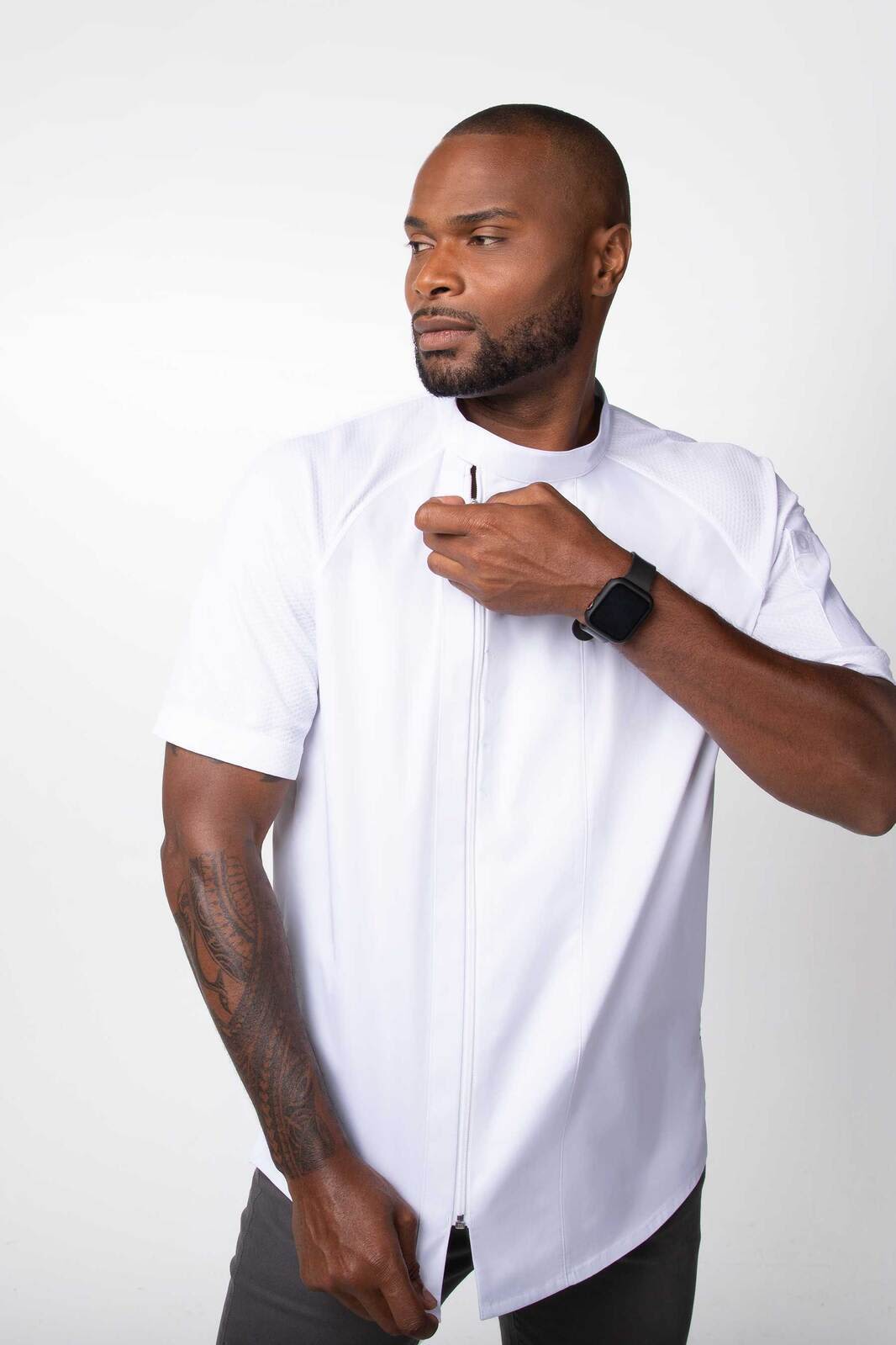 A man wears a short-sleeved, white chef jacket with a zip, showcasing a modern design. It features a branding logo.