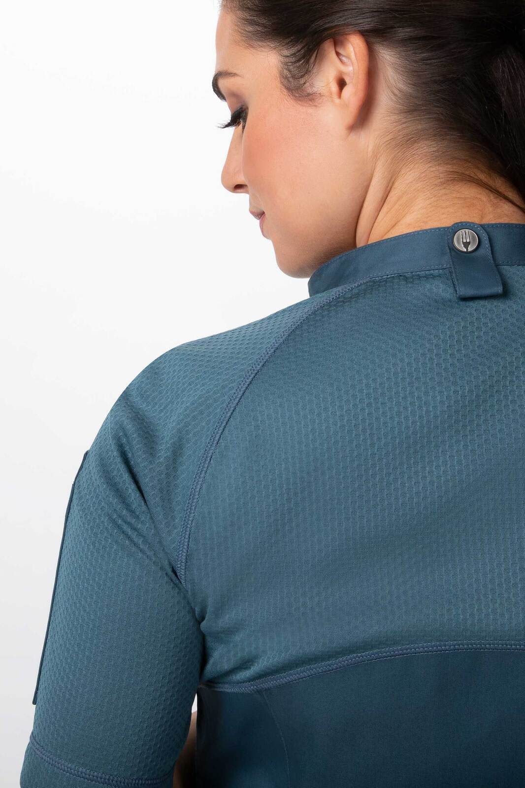 A women's chef jacket in teal, featuring a textured design and a rear button closure. Includes a brand logo.