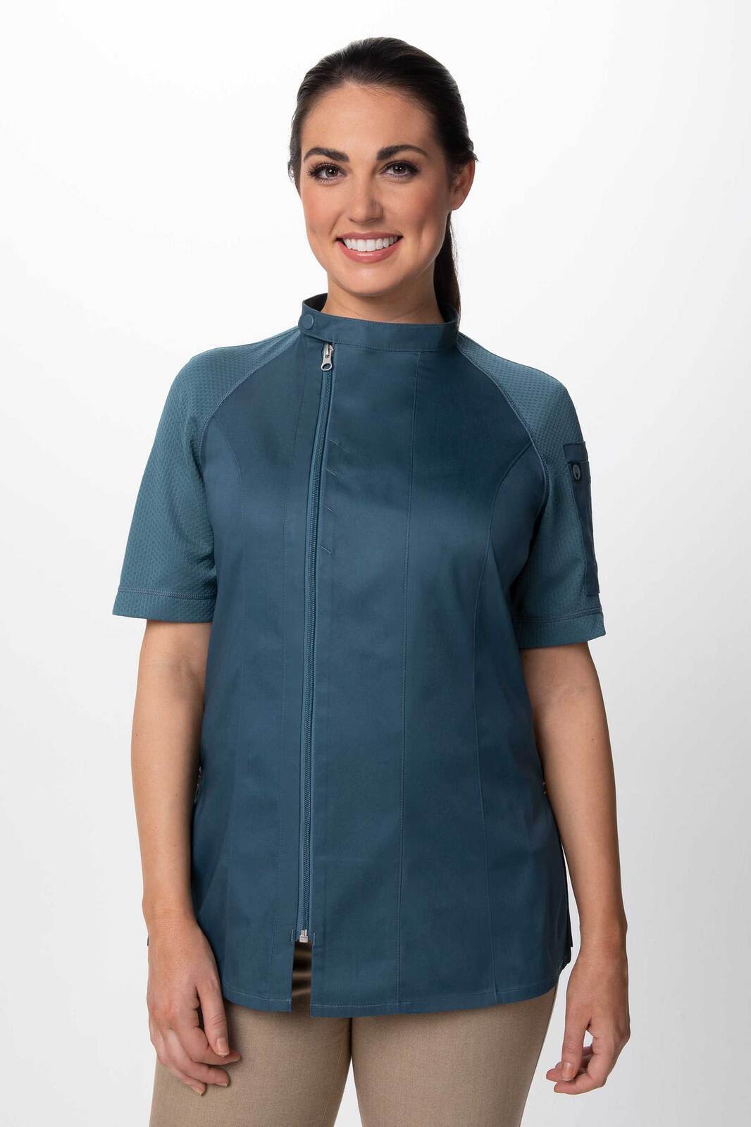 A woman wearing a teal chef jacket with short sleeves and a zip front. The jacket features a logo on one sleeve.