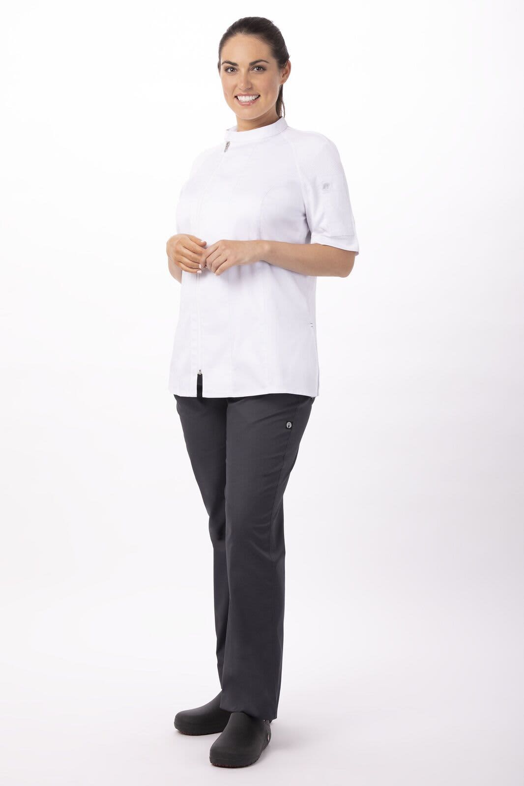 A woman is wearing a white chef jacket with short sleeves and black chef pants, standing on a plain background.