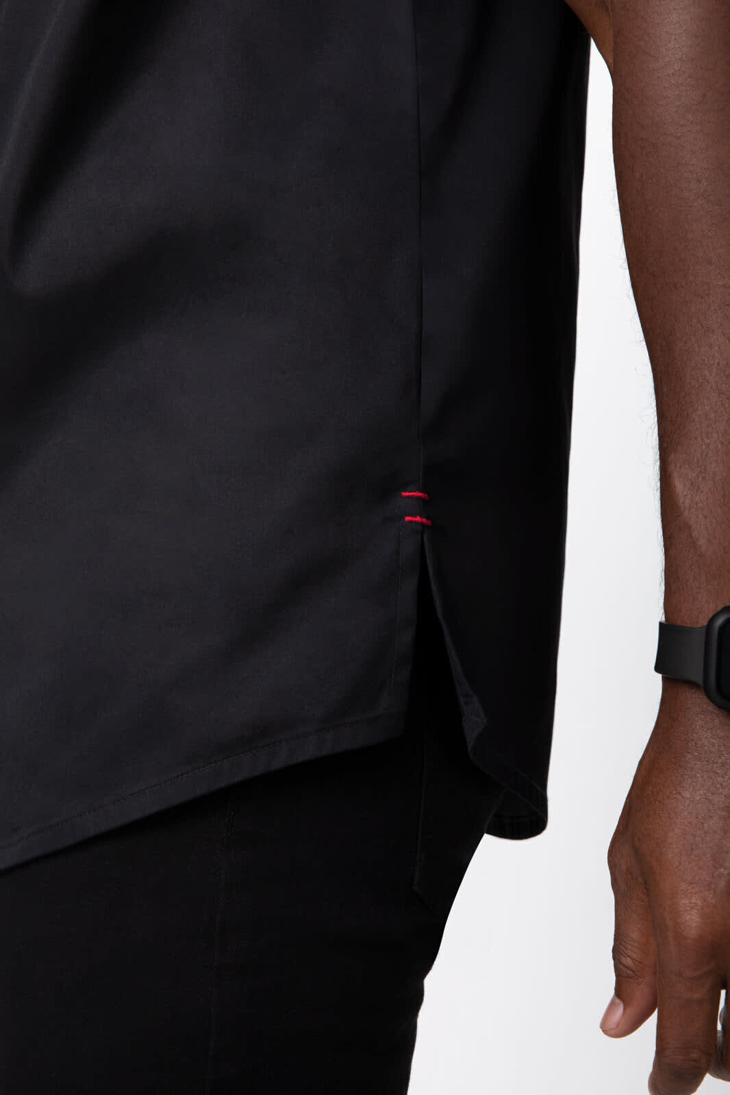 A black chef jacket featuring a side split detail and subtle red stitching, with a logo on the chest.