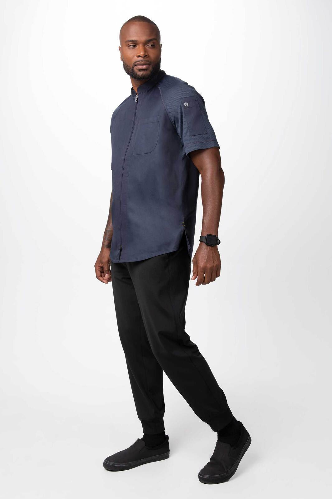 A navy chef jacket worn by a man, paired with black pants and shoes, featuring a logo on the sleeve.