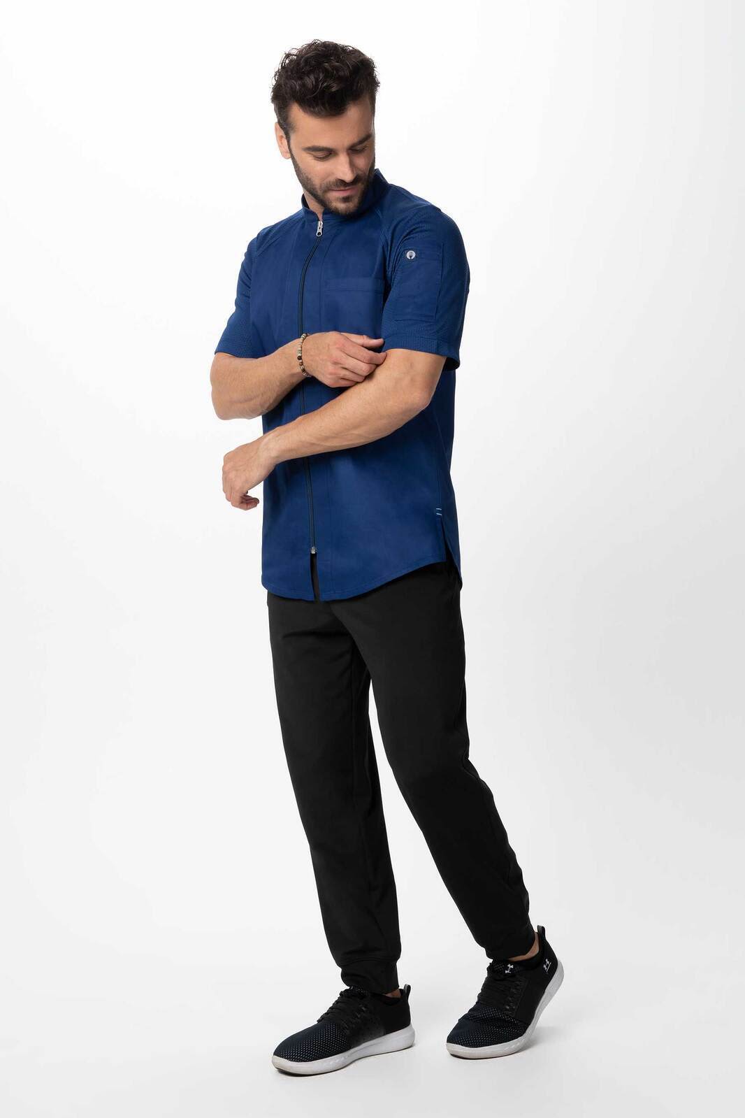 A navy blue men's chef jacket with short sleeves, worn with black pants and black sneakers. The jacket has a logo.