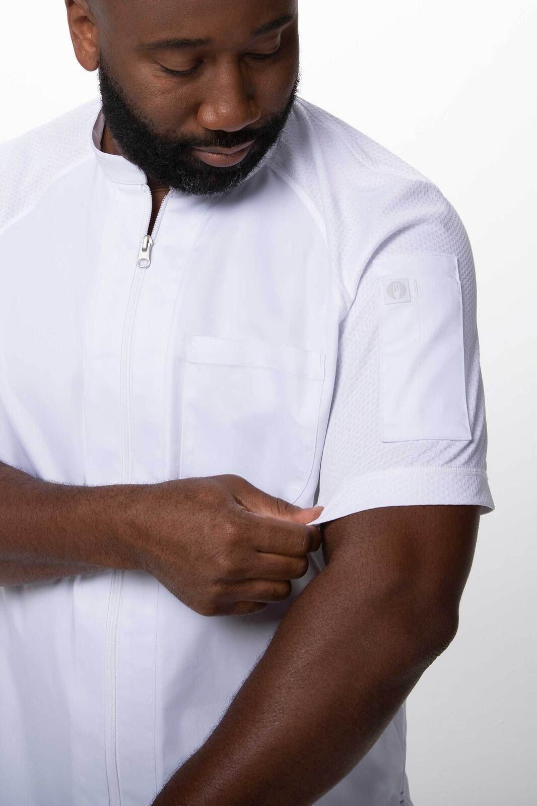 A man wearing a white chef jacket with a zip and short sleeves, featuring a logo on the shoulder.