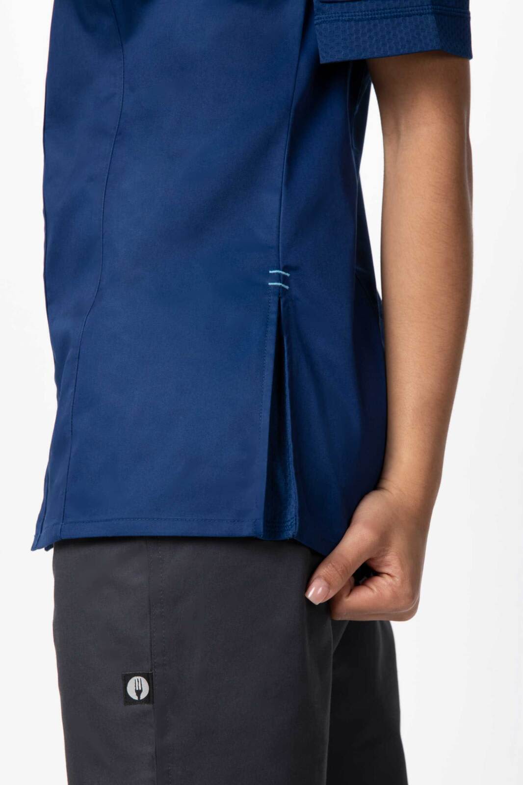 A navy women's chef jacket featuring side vents and a partial view of a hand holding the garment. The jacket has a logo.