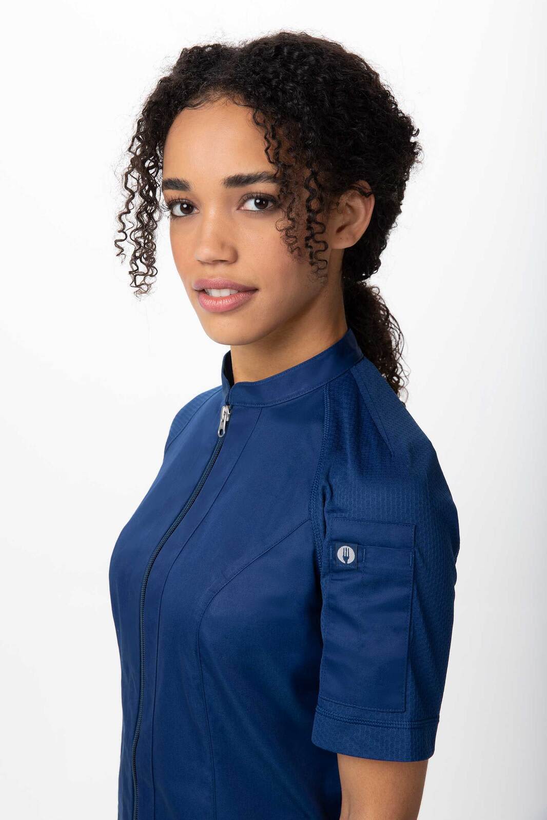 A women's chef jacket in navy blue, featuring short sleeves and a zippered front. It has a small logo on the sleeve.