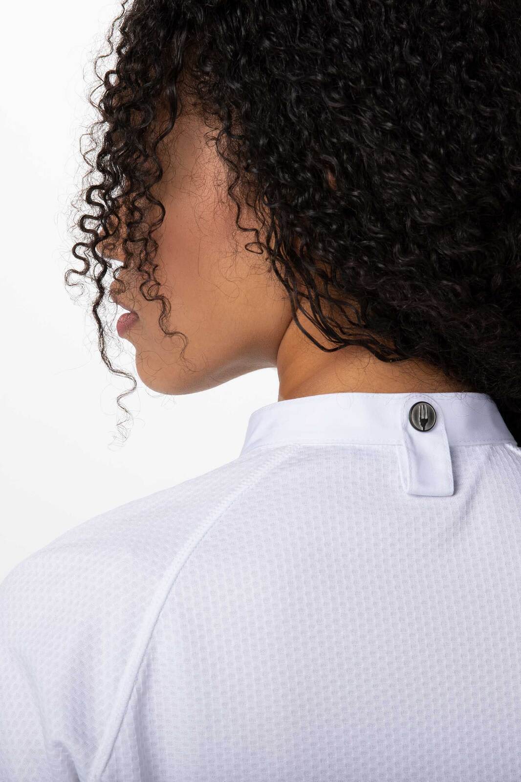 A woman with curly hair is wearing a white chef jacket, featuring a button at the back of the collar.